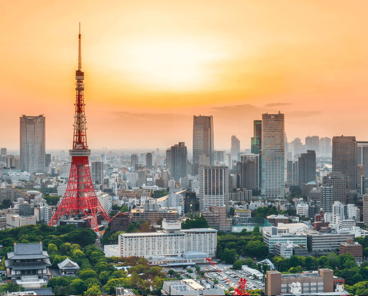 Tokyo Tower stands tall against a sunset, surrounded by city buildings and greenery, showcasing urban Tokyo's skyline.